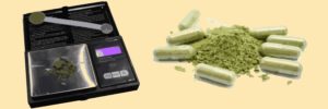 A digital scale with a pile of green powder and a measuring spoon on one side and a pile of green powder and capsules on the other with a yellow background.